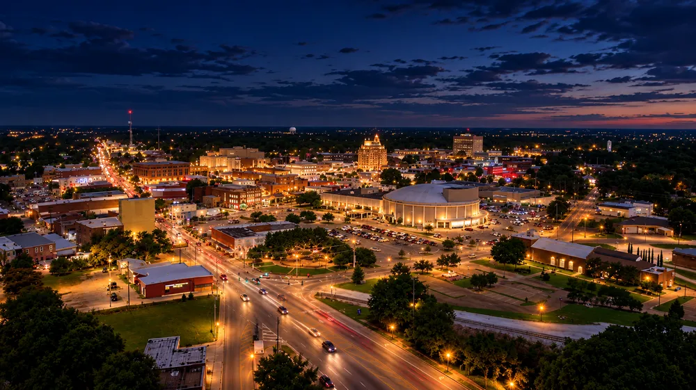 An evening aerial view of downtown Dothan, with lit streets running past low-rise brick storefronts, a domed civic arena and a single tower against a flat horizon